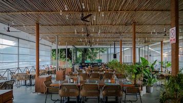 An indoor restaurant with bamboo ceiling, wicker furniture, and potted plants.