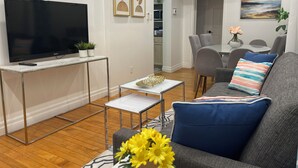 Un salon moderne avec un téléviseur à écran plat, un canapé, une table basse et un coin repas à l’arrière-plan.