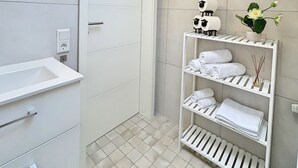 Une salle de bain moderne avec une lucarne, des accessoires blancs et une étagère où sont posés des serviettes et des objets décoratifs.
