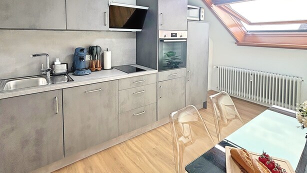 Une cuisine moderne avec des meubles gris, un four encastré et une lucarne.