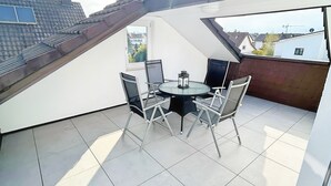 Une terrasse sur le toit, avec une table et des chaises, une vue sur le quartier et un sol carrelé.