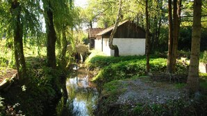 A traditional Japanese-style building with a thatched roof, surrounded by lush greenery and a small stream. - Lička Vodenica Rustical Oasis (Josipdol)