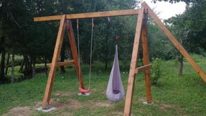 A wooden swing set in a grassy area with trees in the background. - Lička Vodenica Rustical Oasis (Josipdol)