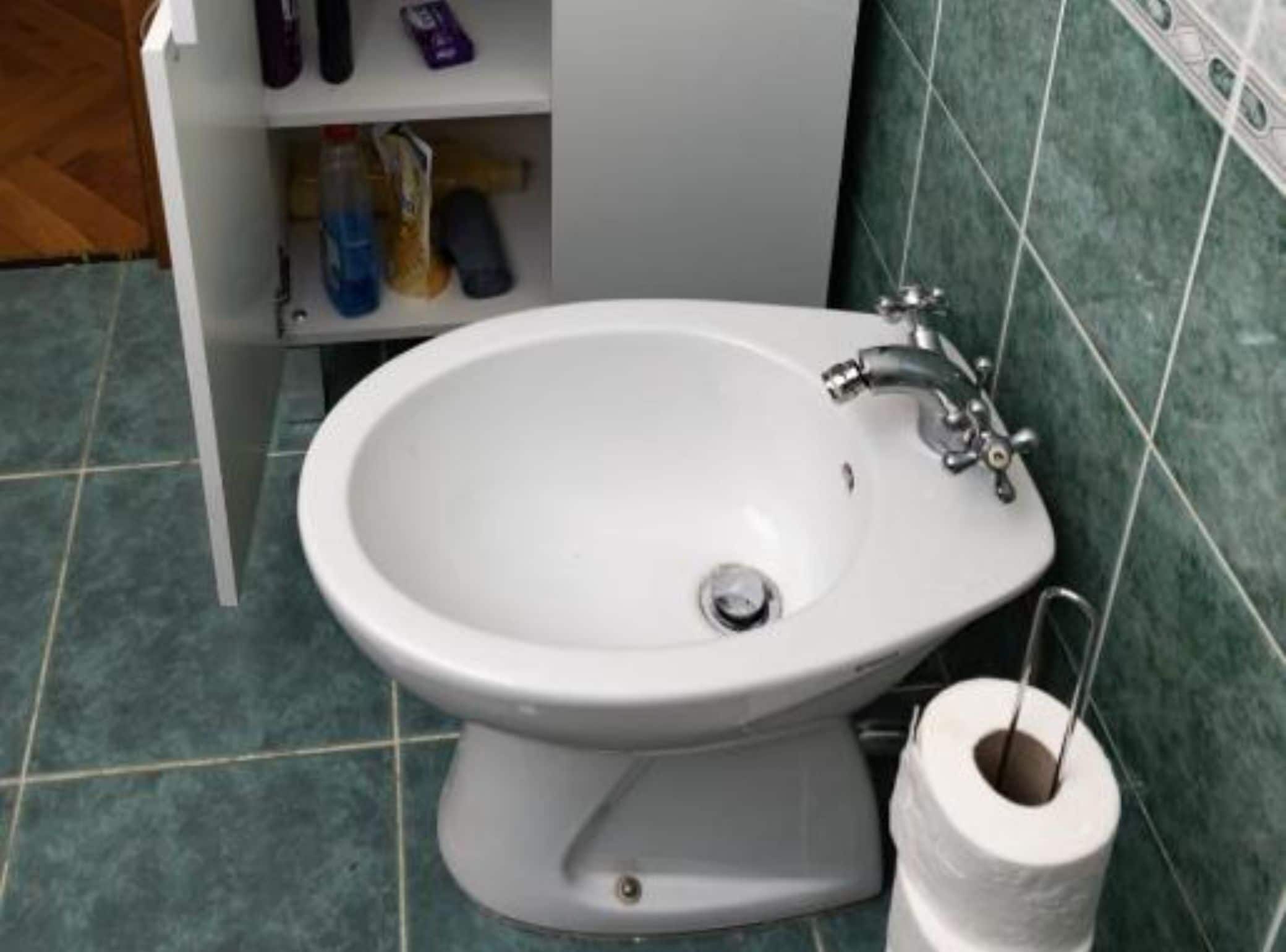 A bathroom with a white sink, a toilet, and a shelf with toiletries.