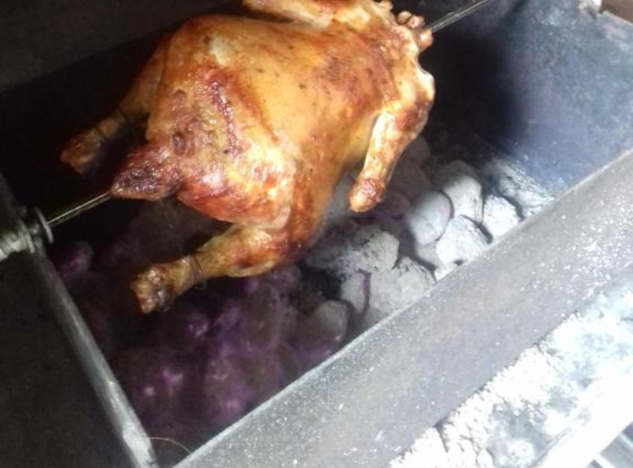 A whole roasted chicken on a spit in a roasting pan.