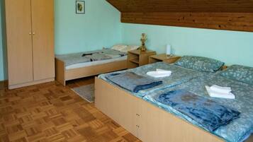 Un dormitorio con un armario de madera, dos camas con ropa de cama azul, suelo de madera y techo de madera.