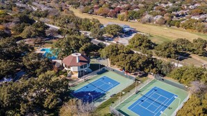An aerial view of a residential area with two tennis courts, a swimming pool, and a house with a distinctive tower. - Work, Explore & Unwind: Convenient San Antonio Gem (San Antonio)