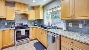 A modern kitchen with wooden cabinets, a stainless steel oven, granite countertops, and a large window providing natural light. - Work, Explore & Unwind: Convenient San Antonio Gem (San Antonio)