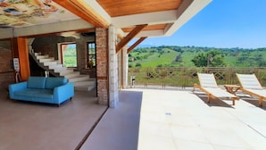 A spacious living area with a blue sofa, a staircase leading to a balcony, and a view of a green landscape.