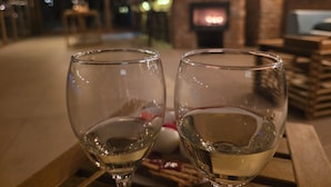 Two empty wine glasses on a wooden table in a dimly lit room with a brick wall and a fireplace in the background.
