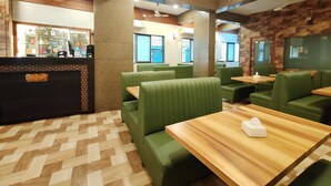 A restaurant with green booths, wooden tables, and a bar area with a display of beverages. - Great Samrat Residency (Khopoli)