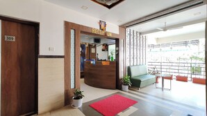 A hotel reception area with a reception desk, a green sofa, potted plants, and a red rug. - Great Samrat Residency (Khopoli)