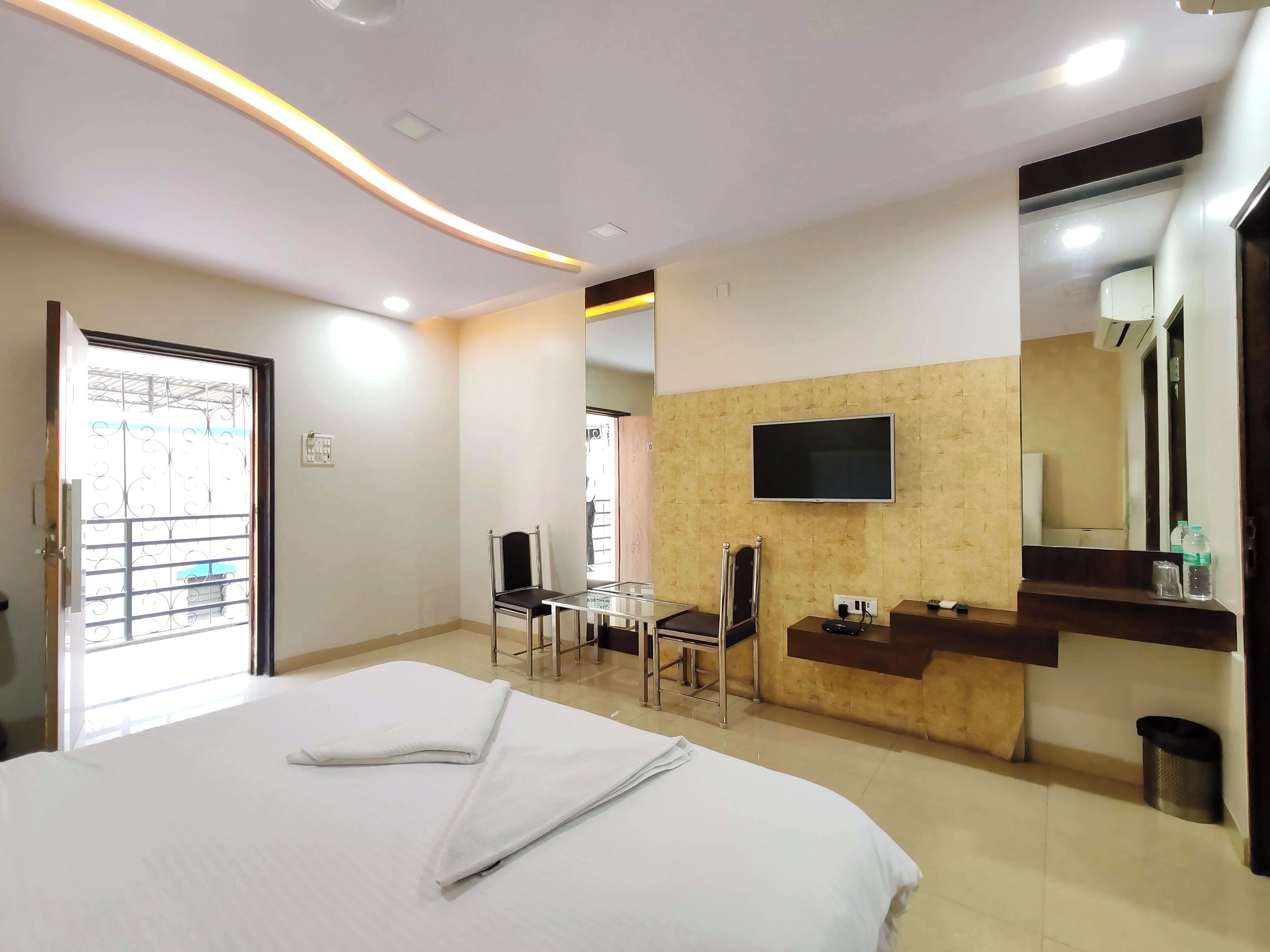 Habitación de hotel con cama, escritorio, silla, televisor montado en la pared y espejo.