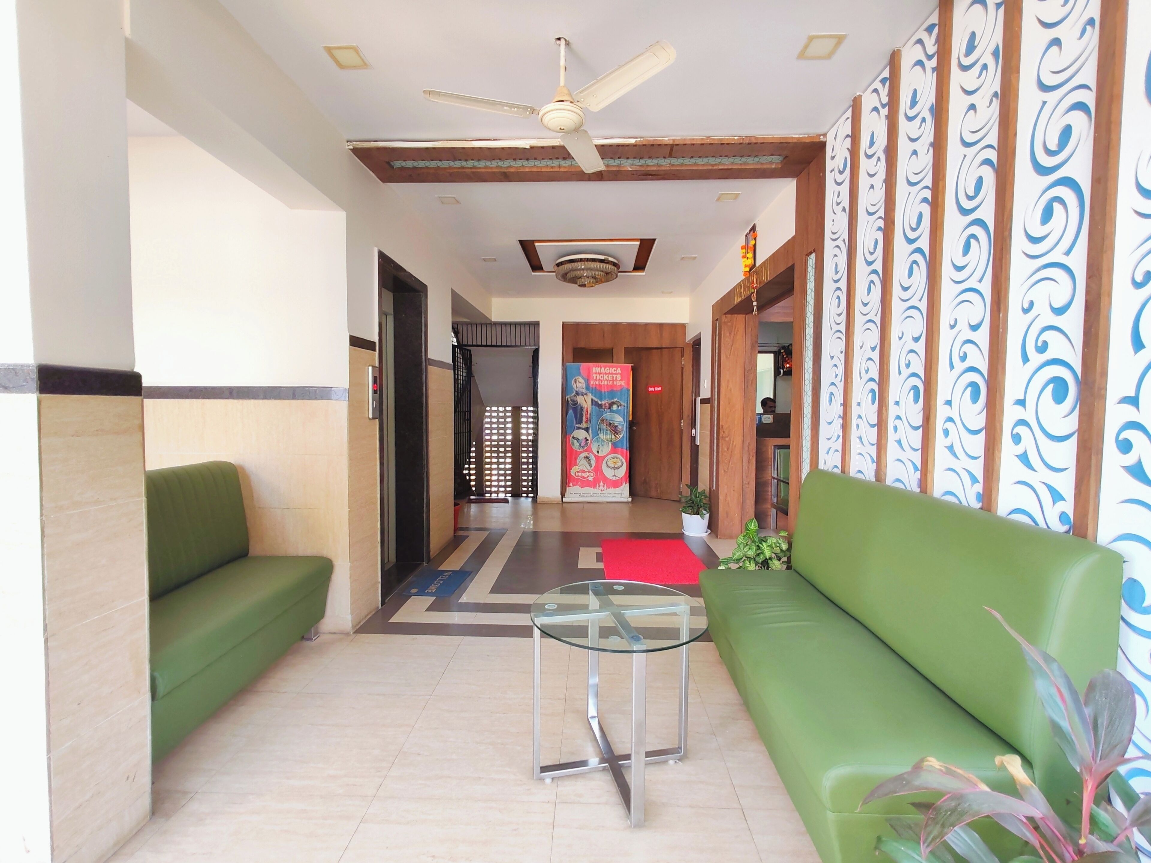 A hotel lobby with green seating, a glass table, a ceiling fan, and patterned walls.