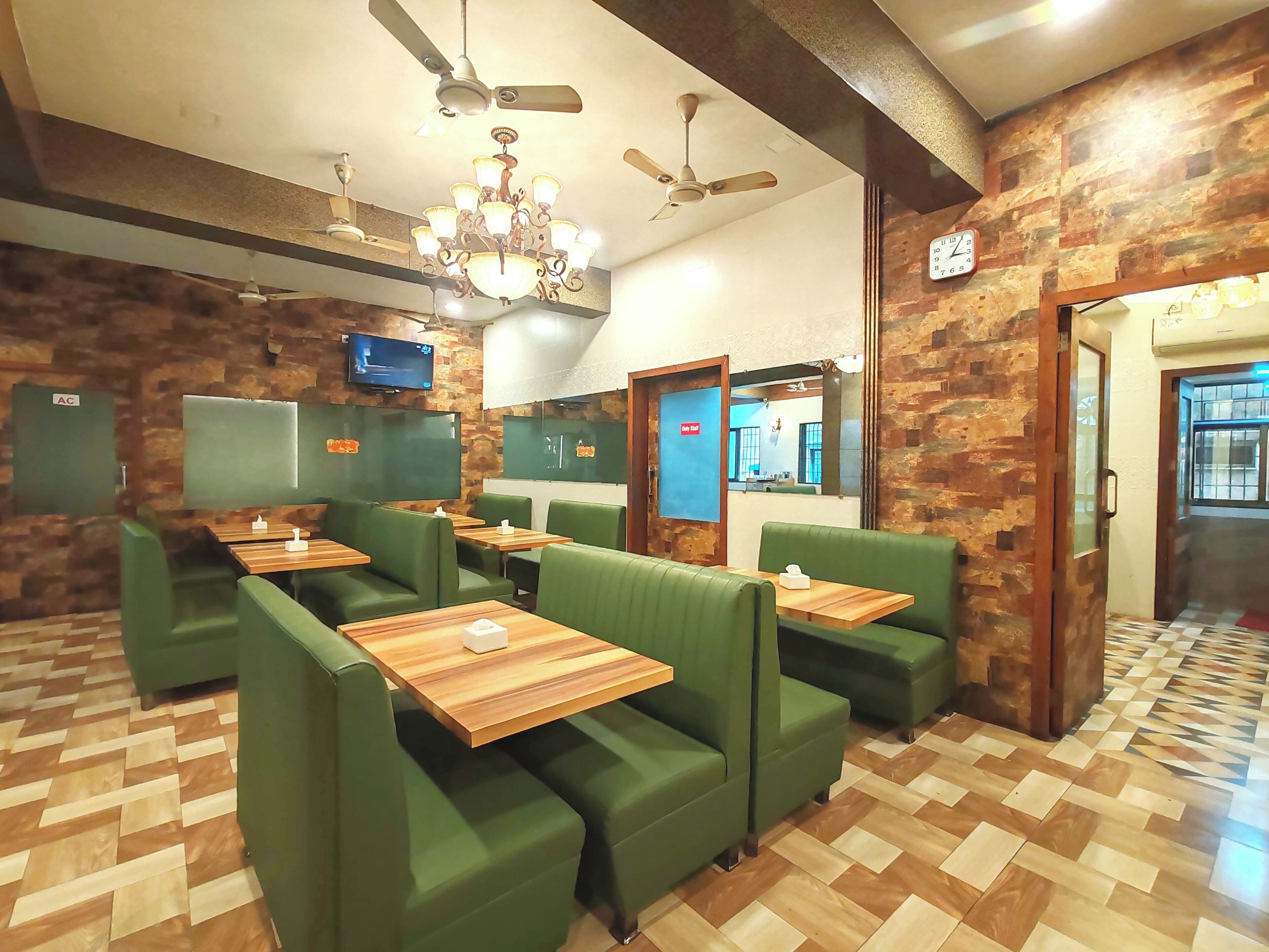 A restaurant with green booths, wooden tables, ceiling fans, and a chandelier.