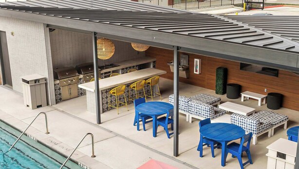 Zona junto a la piscina con barbacoa, asientos y un porche cubierto.