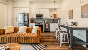 Una cocina moderna con armarios blancos, electrodomésticos de acero inoxidable y una zona de comedor con un taburete de bar y una mesa de madera.