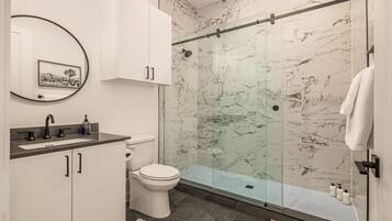 Une salle de bain moderne avec une douche en verre, des toilettes blanches et un lavabo avec un pare-éclaboussures en marbre.