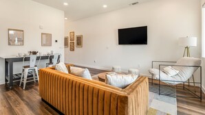 Una sala moderna con sofá, comedor con sillas, televisor en la pared y lámpara.