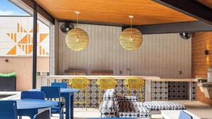 Un área de estar moderna al aire libre con mesas y sillas azules, sillas de mimbre amarillo y cojines estampados.