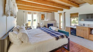 A bedroom with a large bed, wooden ceiling beams, a fireplace, a TV, and a small kitchenette. - Ski, Hike & Fish! Beautiful Retreat Near Taos (Valdez)