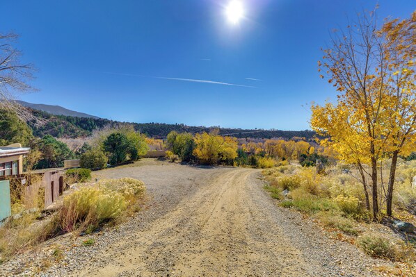 A gravel road leading through a rural area with autumn foliage, a clear sky, and distant hills. - Ski, Hike & Fish! Beautiful Retreat Near Taos (Valdez)