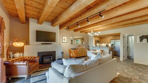 A spacious living room with a fireplace, a television mounted on the wall, and a kitchen area visible through an open door. - Ski, Hike & Fish! Beautiful Retreat Near Taos (Valdez)