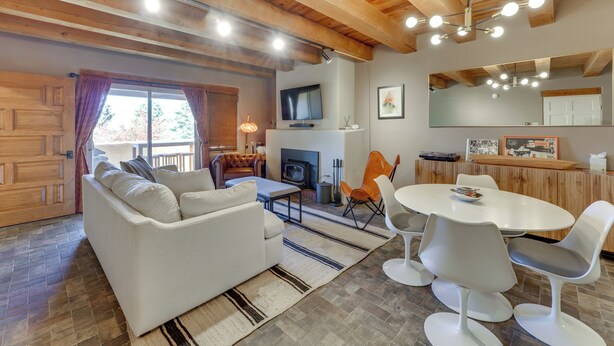 A cozy living room with a fireplace, a television, and a dining area with modern chairs and a table. - Ski, Hike & Fish! Beautiful Retreat Near Taos (Valdez)