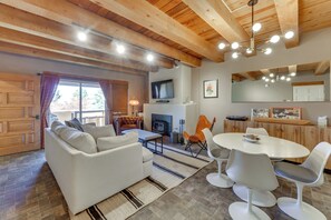 A cozy living room with a fireplace, a television, and a dining area with modern chairs and a table. - Ski, Hike & Fish! Beautiful Retreat Near Taos (Valdez)