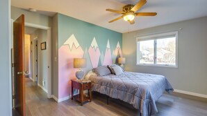 Un dormitorio con cama, ventilador de techo, ventana y una pared decorada con un diseño de montaña.