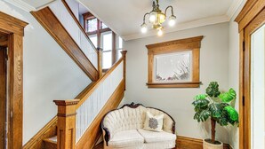 Una escalera con barandillas de madera, un sofá tapizado en blanco con un cojín decorativo y una planta en maceta.