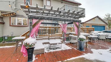 A covered patio area with outdoor seating, a wooden pergola, and a brick floor.