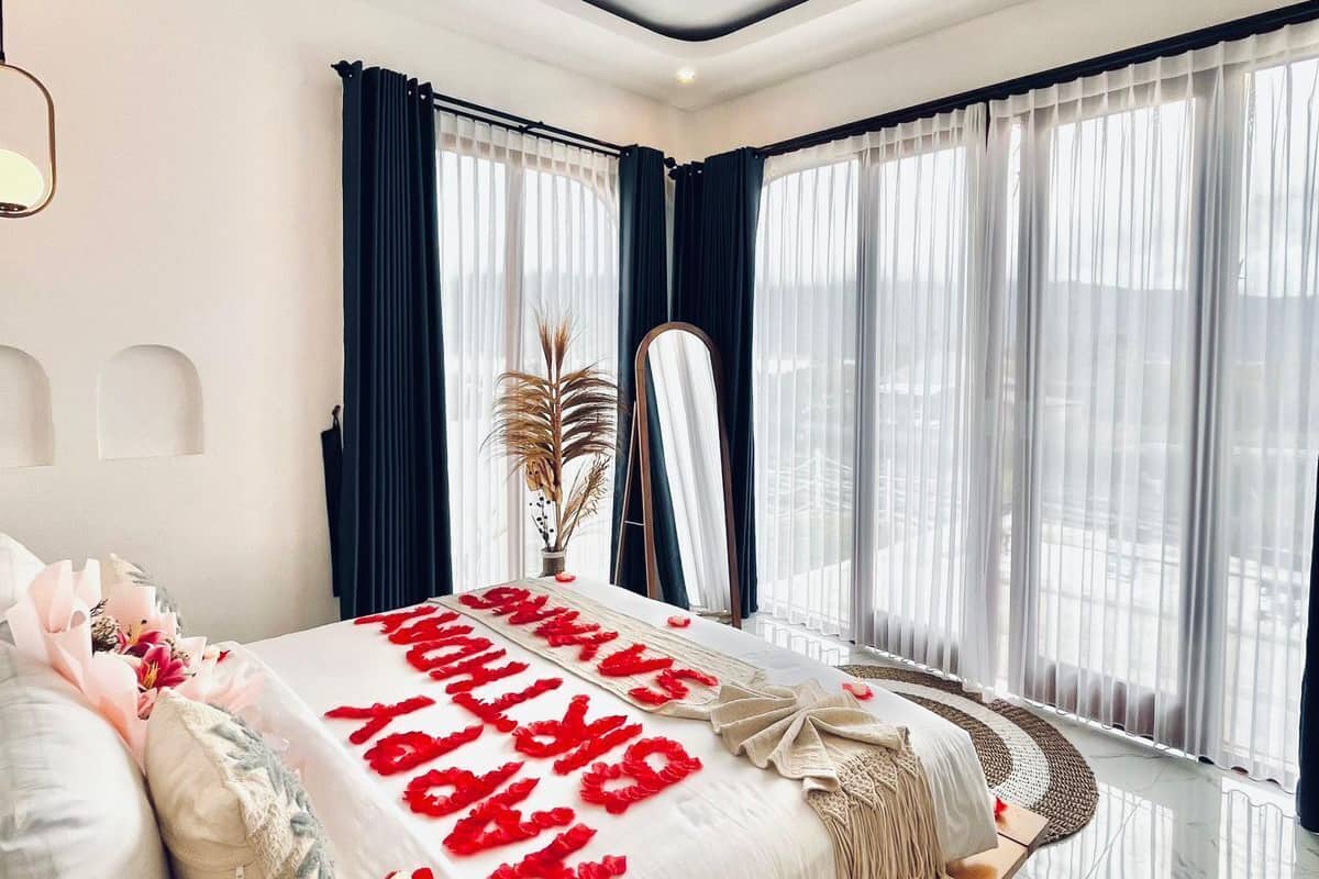 Une chambre moderne avec un grand lit, un miroir et une vue sur la ville grâce à de grandes fenêtres.