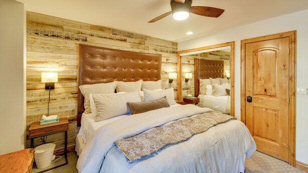 Une chambre à coucher avec un grand lit, une tête de lit en bois, des tables de chevet, un ventilateur de plafond et une porte en bois.