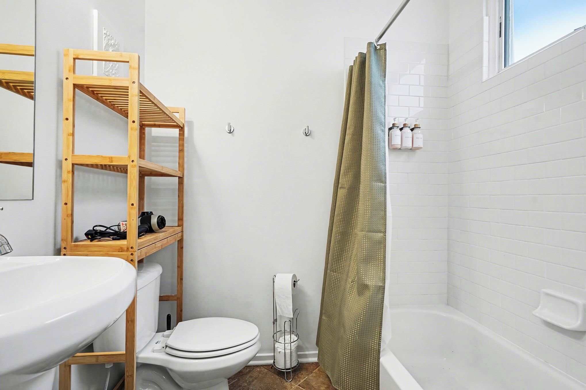 A bathroom with a wooden shelf, toilet, sink, and shower curtain.