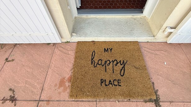 Ein Durchgang zu einem Essbereich mit Tisch und Stühlen, einer Fußmatte mit der Aufschrift 'MY happy PLACE' und einem gefliesten Boden.
