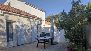 Eine Terrasse mit Tisch und Stühlen, ein weißes Gebäude mit einem Ziegeldach und ein Blumentopf.