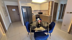 A modern kitchen with stainless steel appliances, a dining area with a glass table and blue chairs, and a hallway leading to a door. - Royale Highend  Burj and Fountain View (Dubai)
