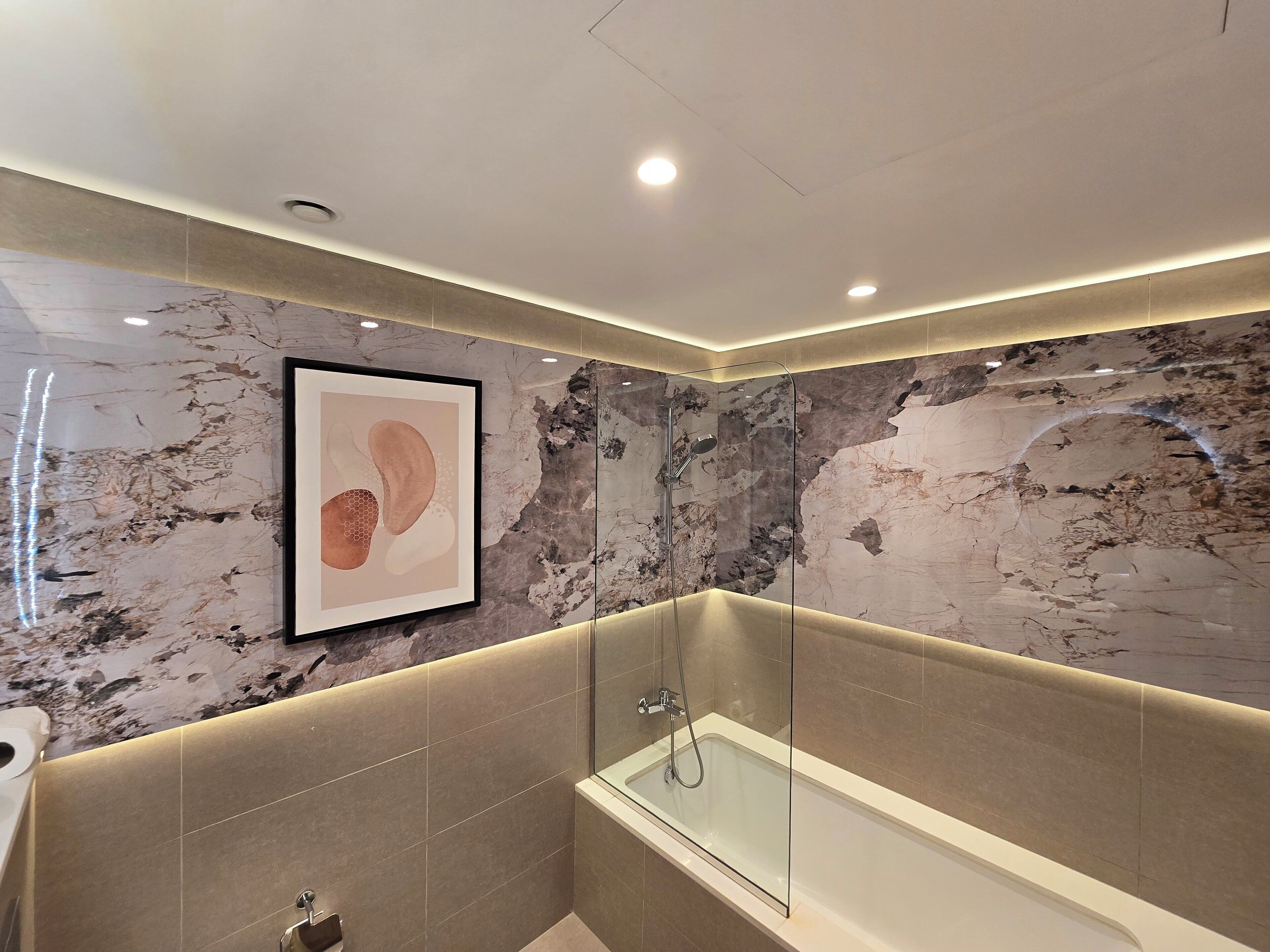 A modern bathroom with a glass-enclosed bathtub, marble walls, and recessed ceiling lighting.