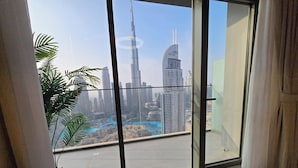 A view from a balcony with a glass door, overlooking a cityscape with high-rise buildings and a river. - Royale Highend  Burj and Fountain View (Dubai)
