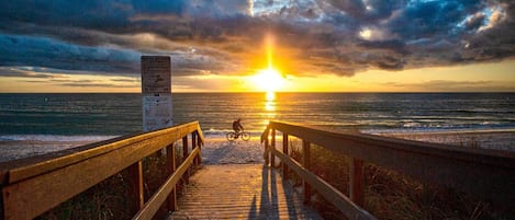 Un paseo marítimo de madera que conduce al océano, con un atardecer de fondo.