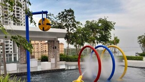 A water feature with a yellow and blue control panel, surrounded by greenery and buildings.