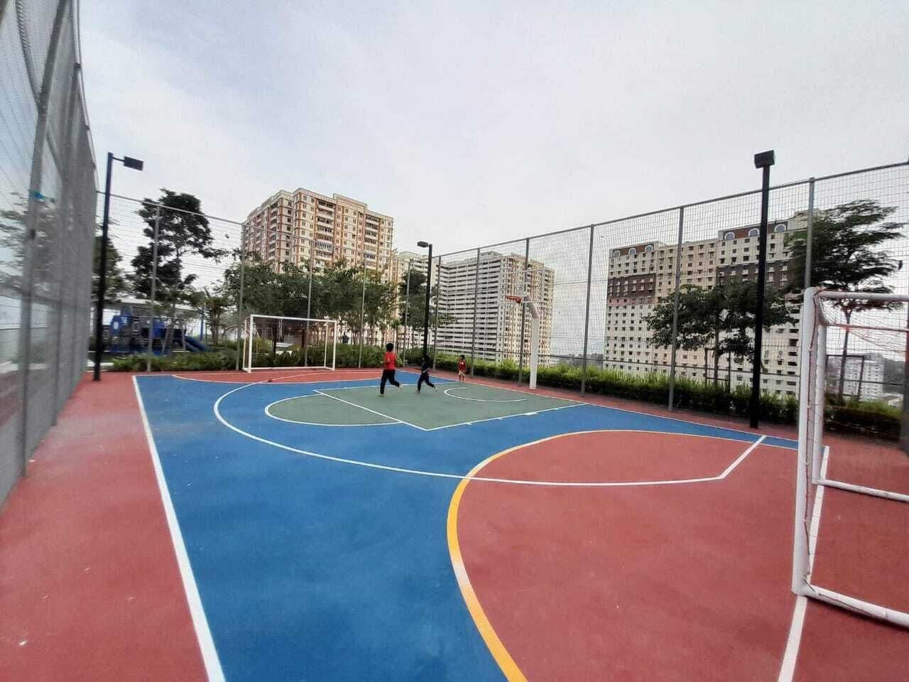 An outdoor basketball court with a red, blue, and green playing surface, surrounded by a fence.