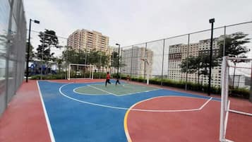 An outdoor basketball court with a red, blue, and green playing surface, surrounded by a fence.