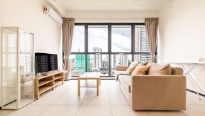 Ein modernes Wohnzimmer mit großem Fenster, einer Couch, einem Couchtisch und einem Fernseher auf einem Lowboard.