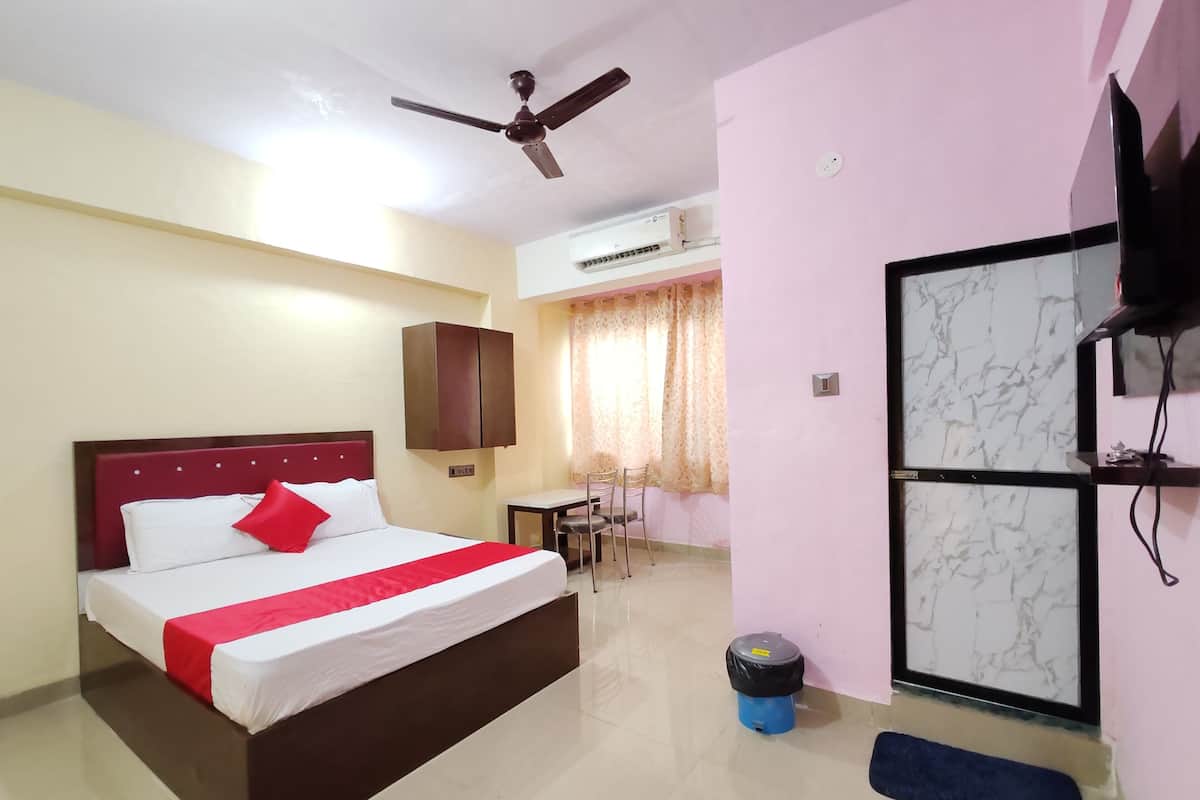 Una habitación de hotel con cama, escritorio, silla, ventilador de techo, aire acondicionado y televisor en la pared.