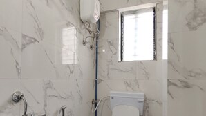 A bathroom with a toilet, a shower, and a hand dryer. - Hotel Pallavi Inn (Panvel)