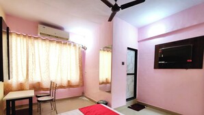 A room with a bed, a desk, a chair, a ceiling fan, and a TV mounted on the wall. - Hotel Pallavi Inn (Panvel)