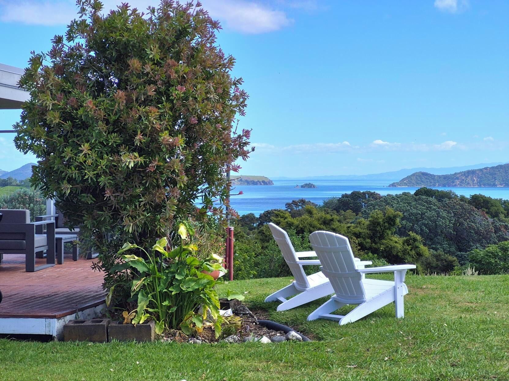 Una terraza con sillas Adirondack que ofrece vistas panorámicas del océano y las colinas.