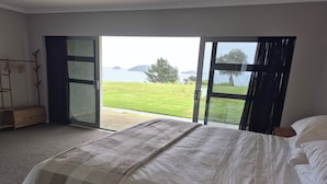 A bedroom with a bed, a wooden dresser, and a view of a grassy area and water through a glass door.